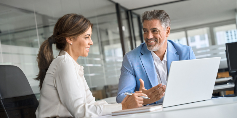 Professional bank manager consulting company client on financial taxes. Two middle aged professional executives team business people working together on laptop computer at office corporate meeting.