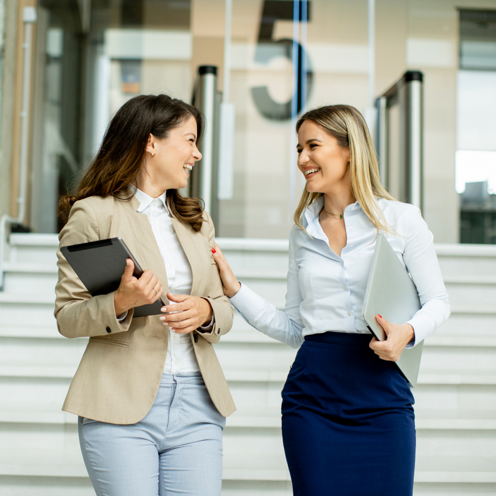 Two cute young business women walking on stairs in the office hallway